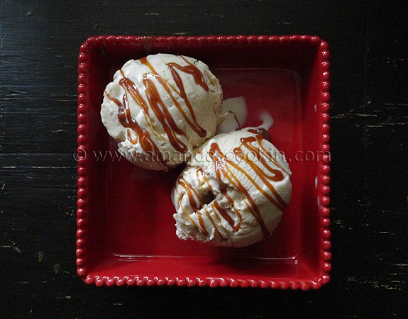 An overhead photo of two scoops of apple cider ice cream in a red dish with caramel drizzled on top. 