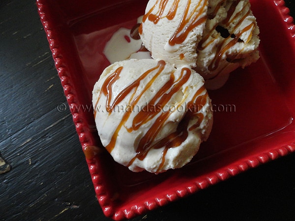 A close up photo of two scoops of apple cider ice cream in a red dish with caramel drizzled on top. 