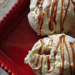 A close up photo of two scoops of apple cider ice cream on a red plate with caramel drizzled on top.
