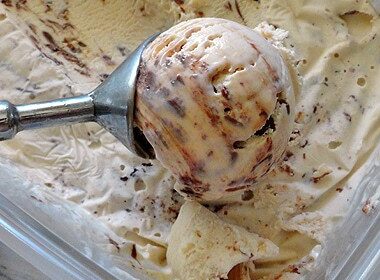 A close up photo of an ice cream scoop scooping Nutella swirl cheesecake ice cream.