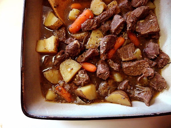 An overhead photo of beef stew with parsley, sage, rosemary and thyme in a square bowl.