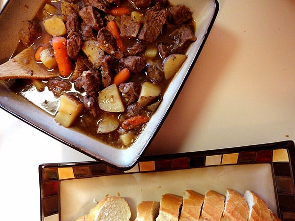 An overhead photo of beef stew with parsley, sage, rosemary and thyme in a square bowl.