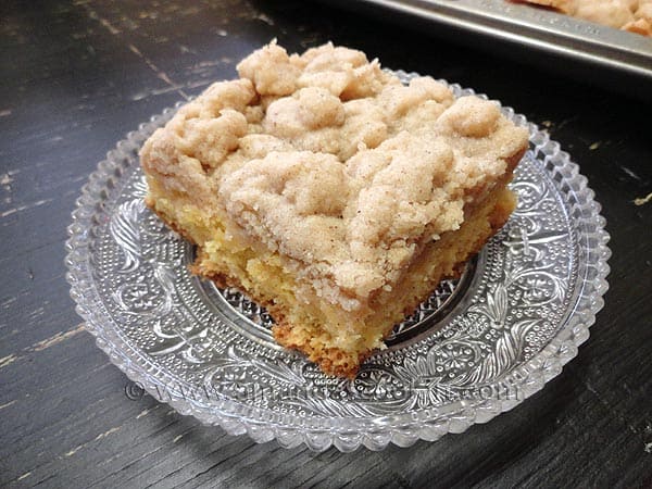 A close up photo of a piece of crumb cake on a clear plate.