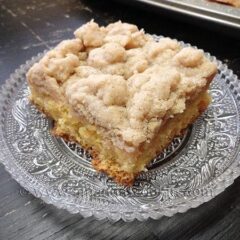 A close up photo of a square of crumb cake on a clear plate.