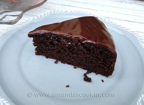 A close up photo of a slice of deep dark chocolate cake on a white plate.