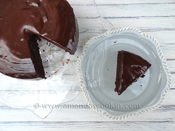 A close up photo of deep dark chocolate cake with a slice on a white plate next to it.