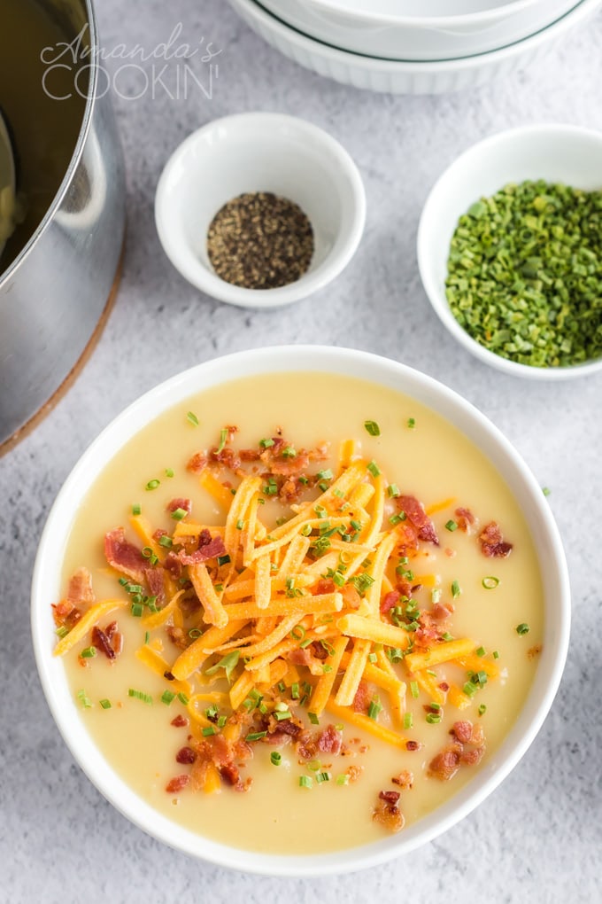 bowl of potato cheese soup with bowl of chives behind it