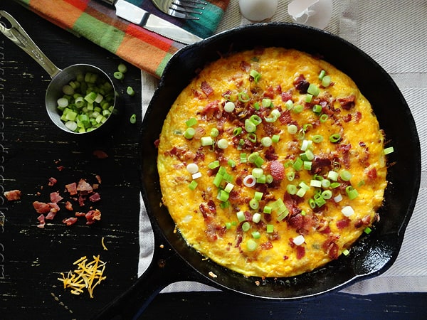 An overhead photo of a cheesy bacon potato frittata in a cast iron pan.