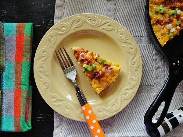 An overhead photo of a slice of cheesy bacon potato frittata on a yellow plate with a fork.