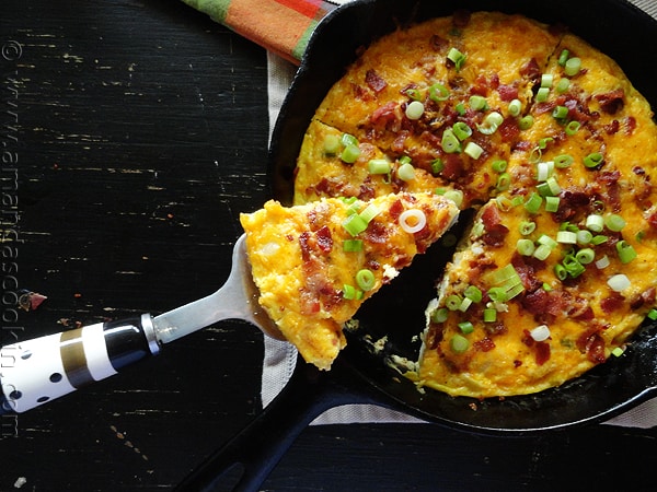 An overhead photo of a slice of cheesy bacon potato frittata being lifted out of the whole pan.