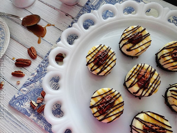 An overhead photo of mini turtle cheesecakes resting on a white decorative platter.