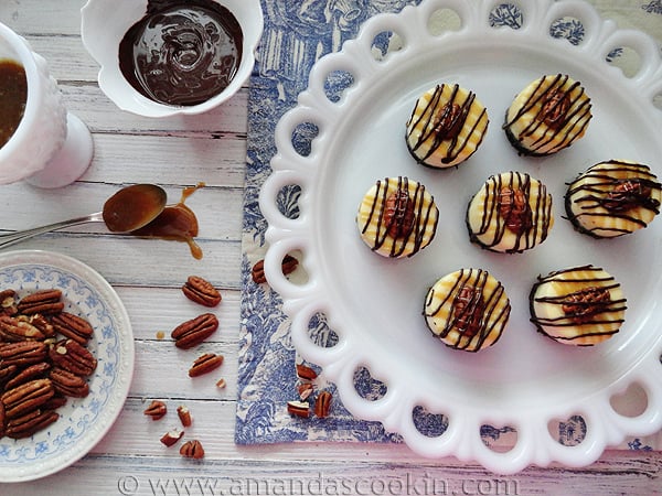 An overhead photo of mini turtle cheesecakes resting on a white decorative platter.