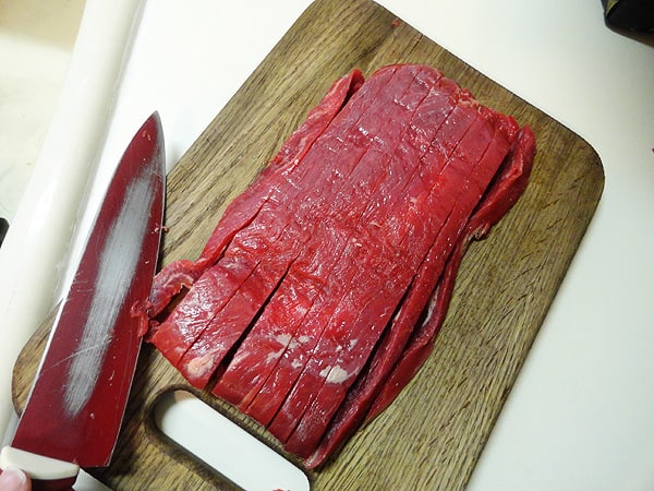 An overhead photo of sliced flank steak on a wooden cutting board. 