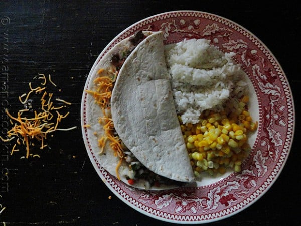 An overhead photo of a steak soft taco on a plate with corn and rice on the side.