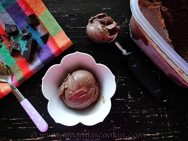 An overhead photo of a scoop of black cow ice cream in a decorative bowl with another scoop in an ice cream scooper to the side.