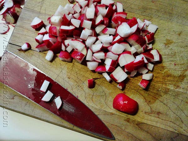 A close up photo of chopped radish on a wooden cutting board with a knife on the side.