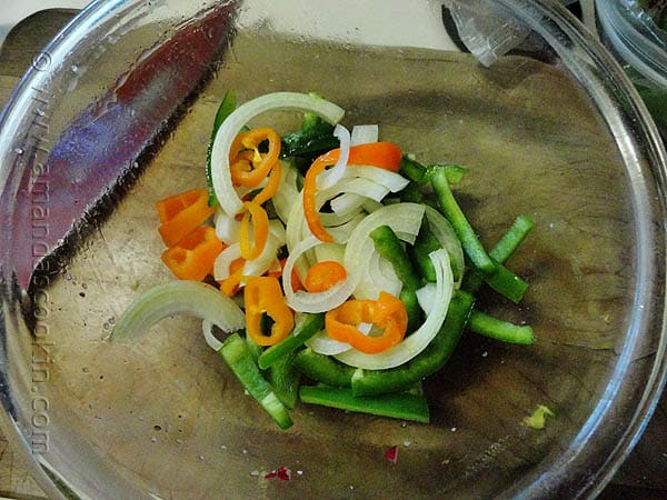 Sliced bell pepper, sweet peppers and onions in a clear bowl.