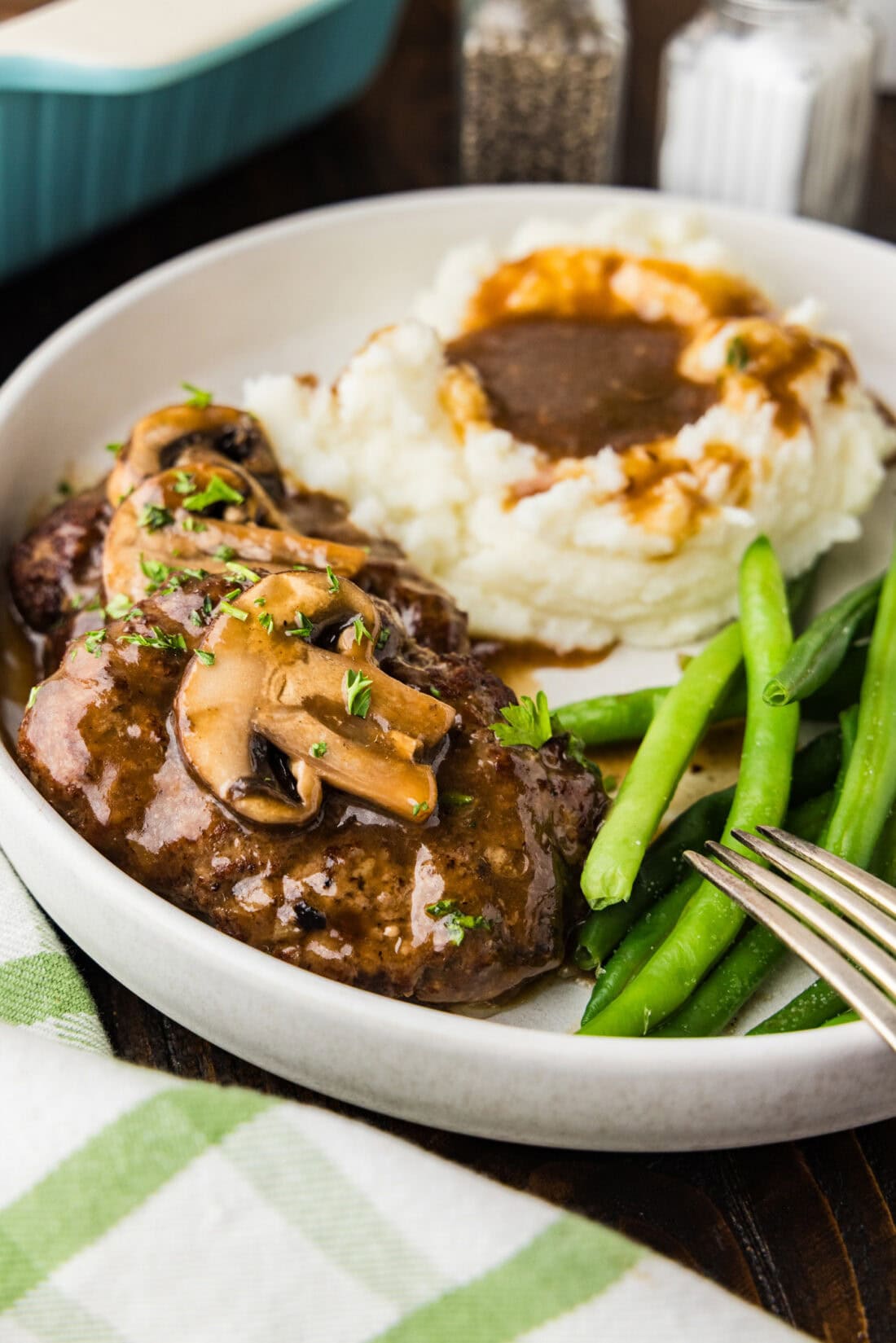 salisbury steak on a plate with mashed potatoes and green beans