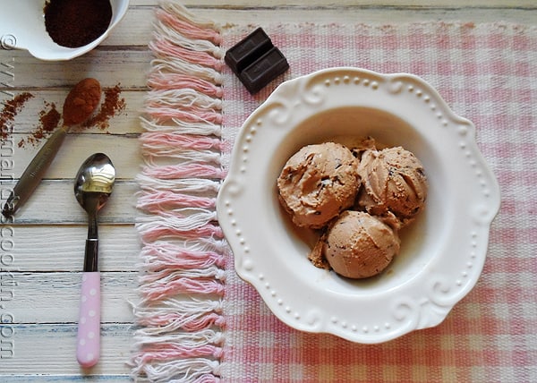 An overhead photo of three scoops of mocha chocolate chip ice cream in a white bowl with a spoon.
