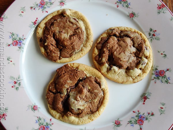 A photo of three half and half chocolate chip cookies resting on a plate.