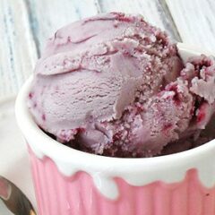 A close up photo of a scoop of vanilla blackberry jam ice cream in a pink bowl.