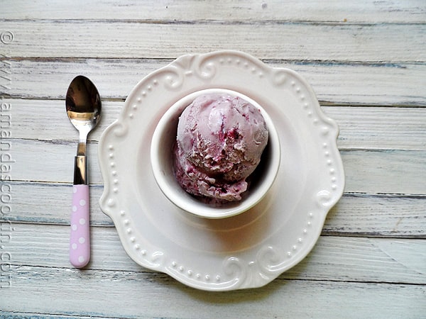 An overhead photo of a scoop of vanilla blackberry jam ice cream in a bowl with a spoon resting to the side.
