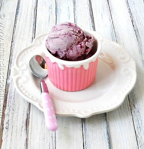 A photo of a scoop of vanilla blackberry jam ice cream in a pink bowl with a spoon resting to the side.
