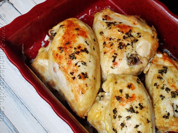 A close up photo of golden roasted chicken breasts in a red roasting pan.