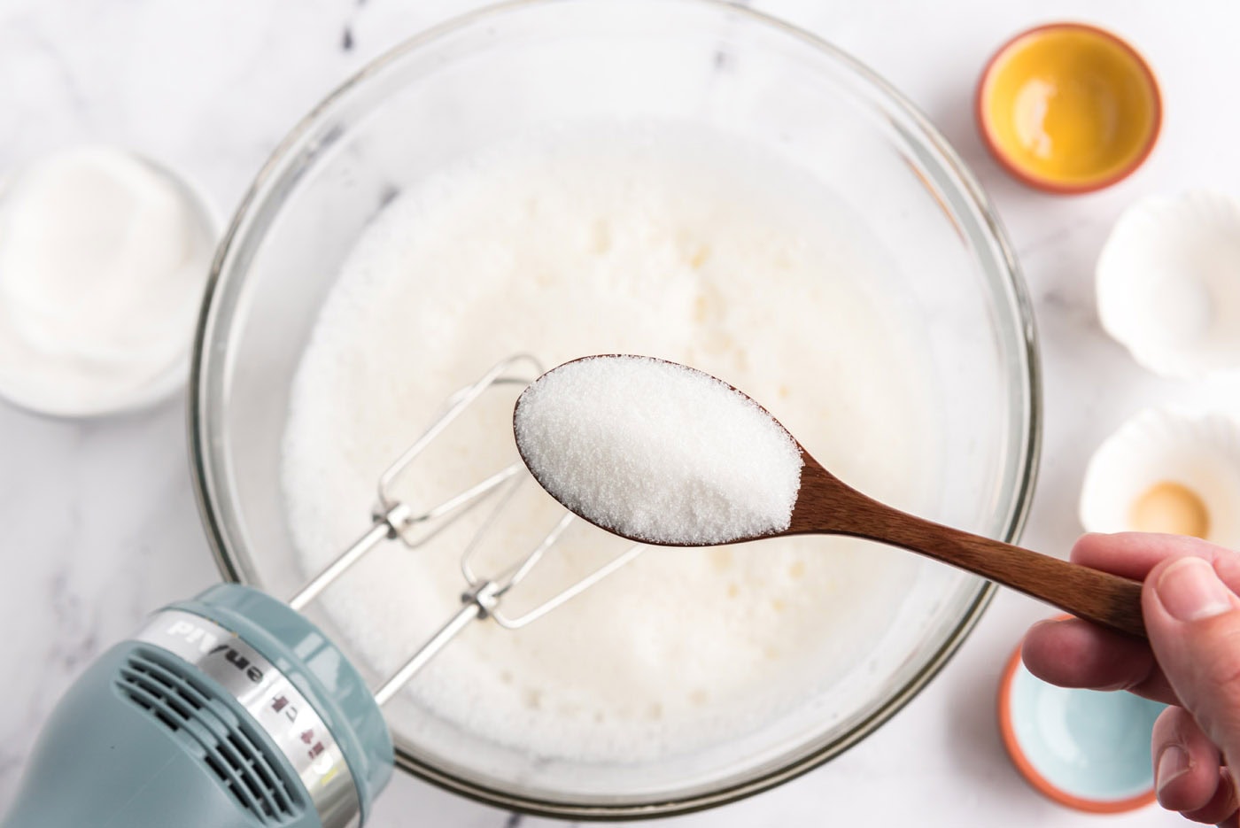 spooning granulated sugar into bowl of egg white mixture