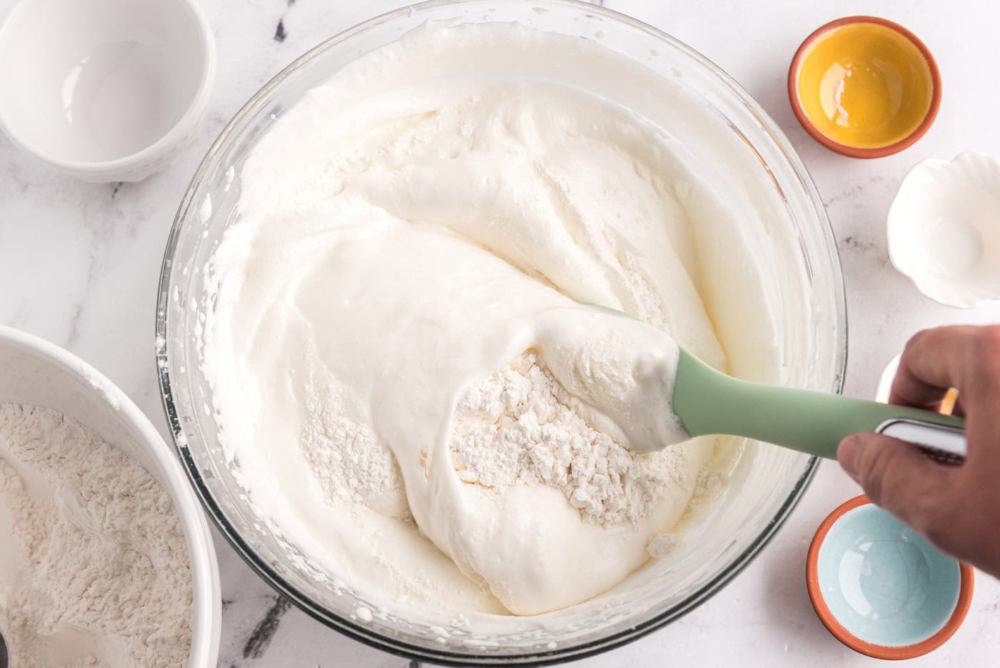 folding flour mixture into egg white mixture in a bowl with a rubber spatula