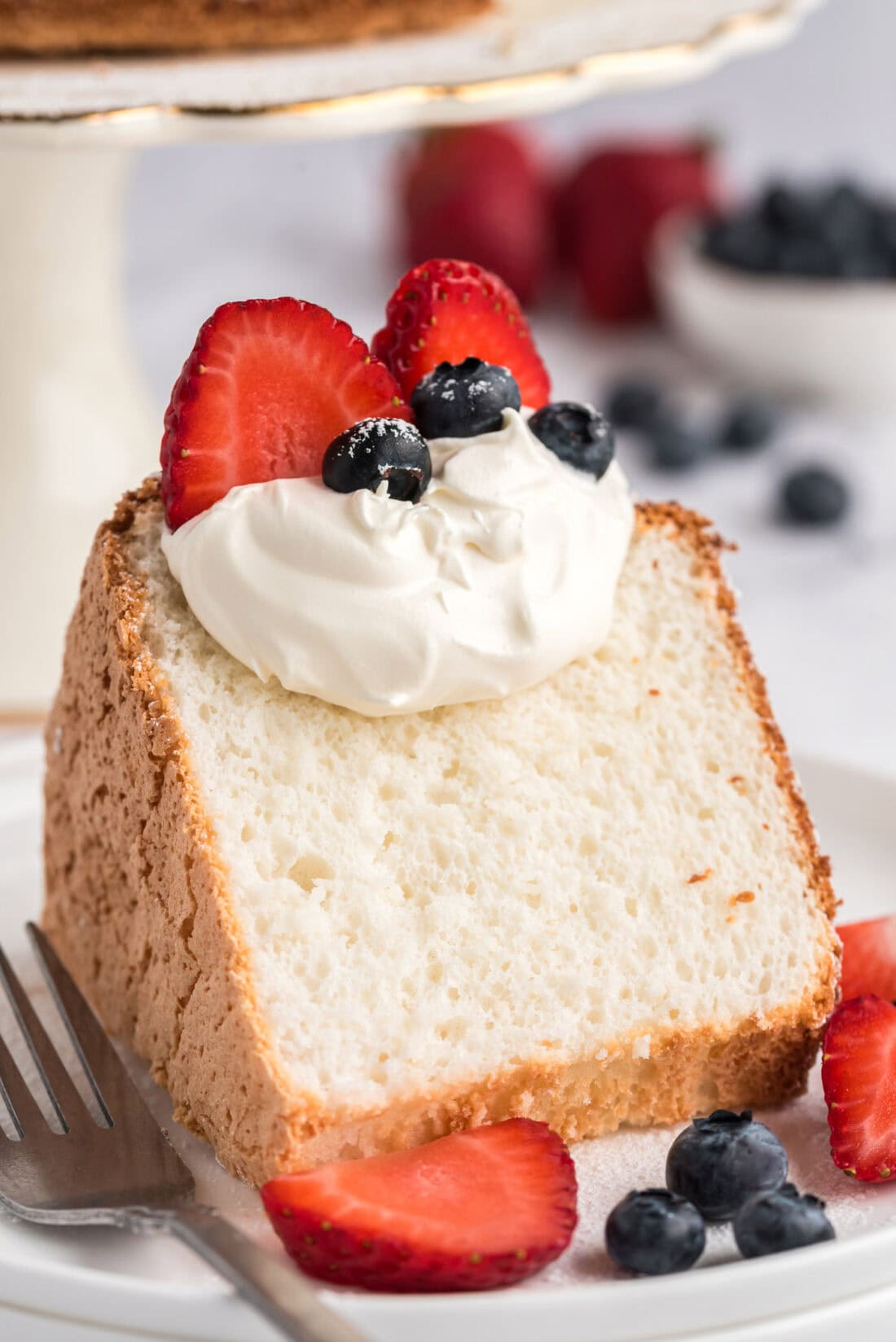 Slice of Angel Food Cake topped with whipped cream and berries