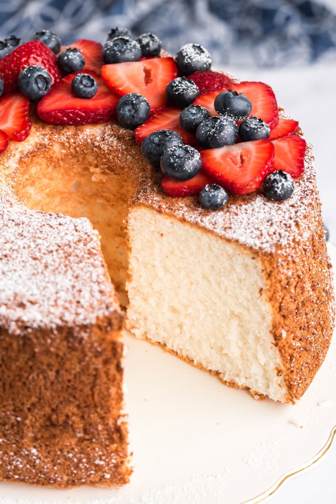 Angel Food Cake topped with powdered sugar and berries with a slice removed