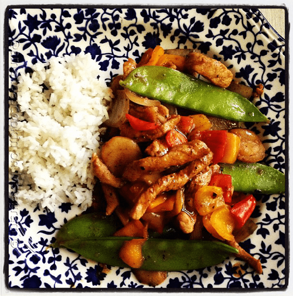 An overhead photo of a plate of peppered pork stir fry with sweet peppers with rice on the side.