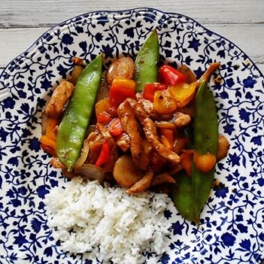 An overhead photo of a plate of peppered pork stir fry with sweet peppers with rice on the side.
