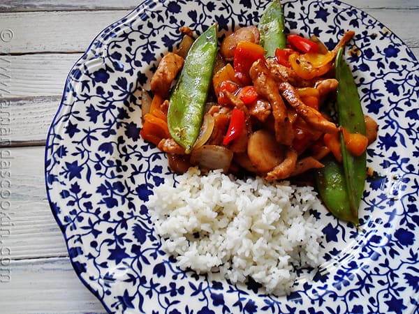 An overhead photo of a plate of peppered pork stir fry with sweet peppers with rice on the side.