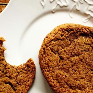 A close up photo of a whole sugar topped molasses spice cookie next to a half eaten cookie on a white plate.