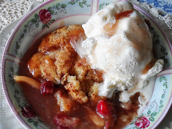 A close up photo of summer fruit crisp in a bowl with ice cream on top.