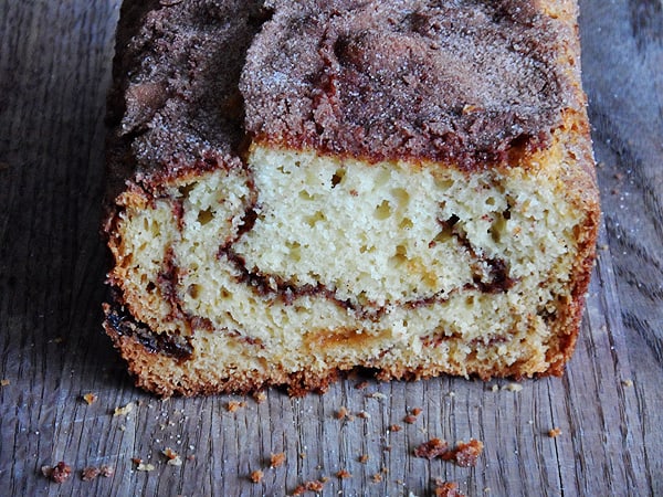 A close up photo of a loaf of cinnamon raisin swirl quick bread cut in half on a wooden cutting board.