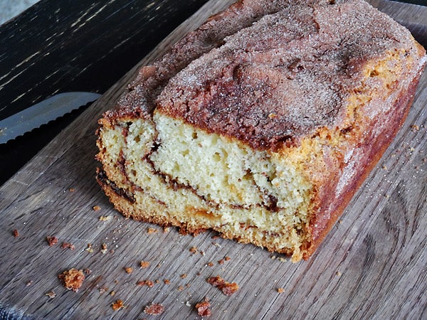 A photo of a loaf of cinnamon raisin swirl quick bread on a wooden cutting board.