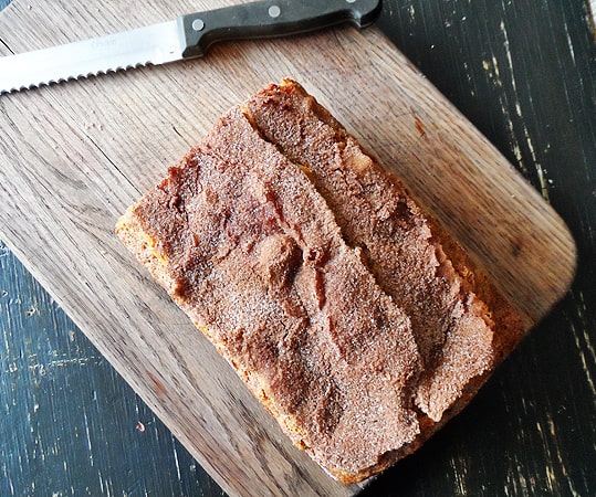 An overhead photo of a loaf of cinnamon raisin swirl quick bread on a wooden cutting board.