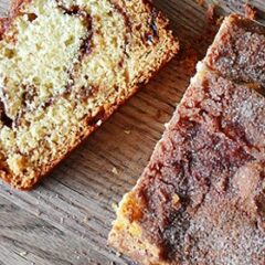 A close up photo of a sliced loaf of cinnamon raisin swirl quick bread on a wooden cutting board.