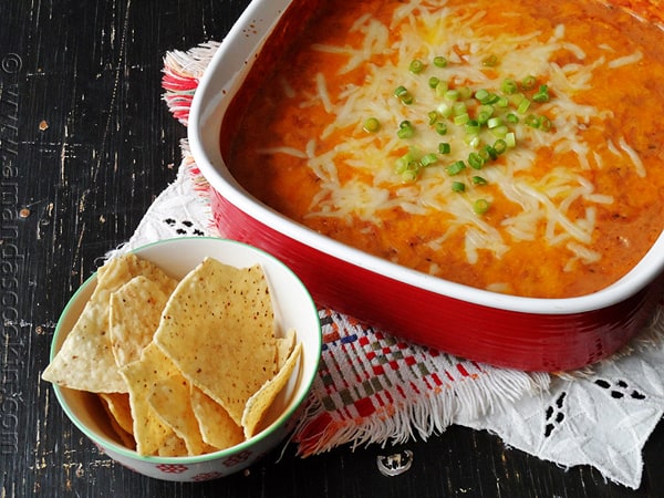 Creamy con queso bean dip in a red bowl with tortilla chips on the side.