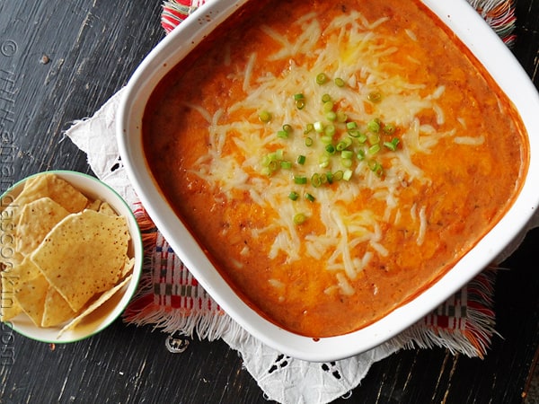 An overhead photo of creamy con queso bean dip in a red dish.