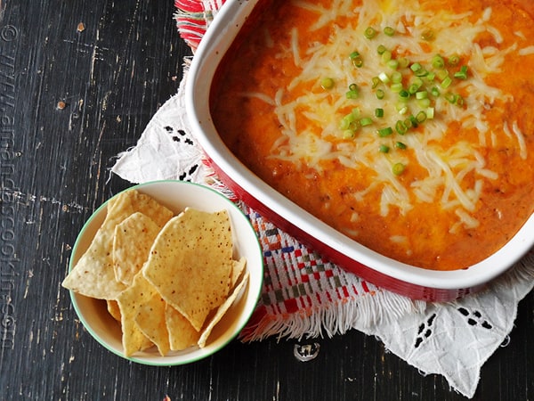 An overhead photo of creamy con queso bean dip in a red dish with tortilla chips on the side.