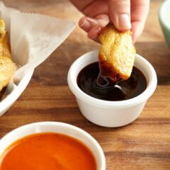 A close up photo of a crispy baked chicken wing being dipped into teriyaki sauce.