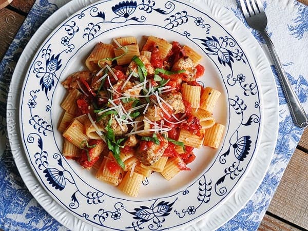 An overhead of a plate of spiced chicken and mezzi rigatoni topped with grated Parmigiano-Reggiano cheese and fresh basil.