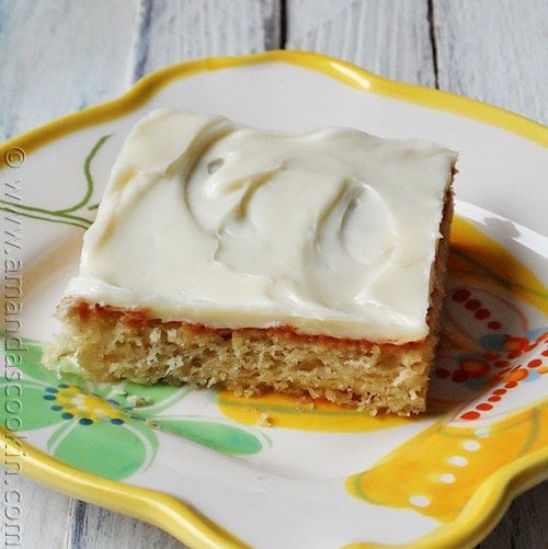 A close up photo of a banana bar with vanilla cream cheese frosting on a white plate.