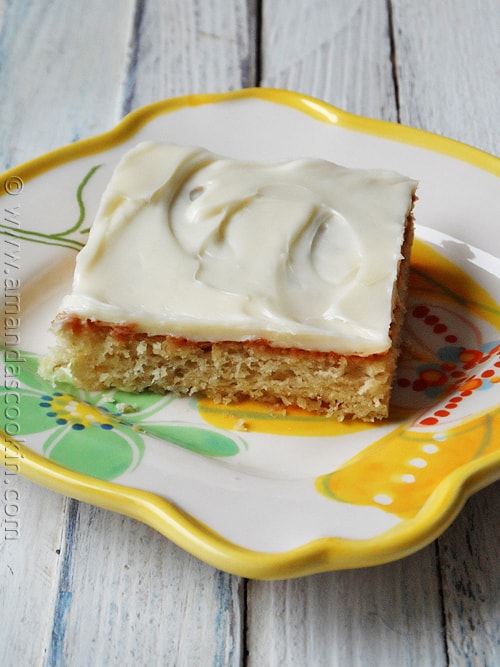 A close up photo of a banana bar with vanilla cream cheese frosting on a plate.