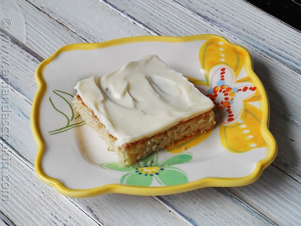 A close up photo of a banana bar with vanilla cream cheese frosting on a plate.