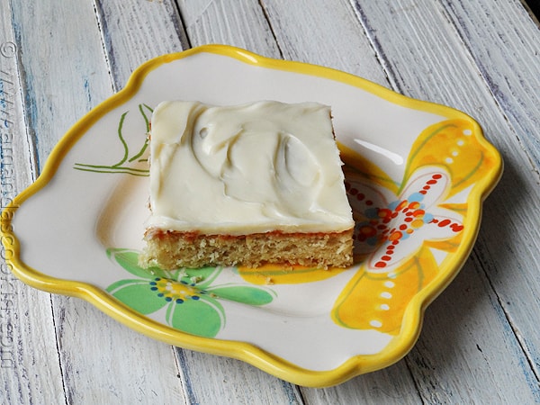 A close up photo of a banana bar with vanilla cream cheese frosting on a plate.